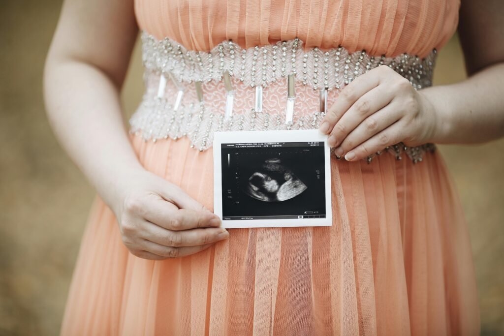 A pregnant woman in a peach dress holds her ultrasound photo, symbolizing motherhood.